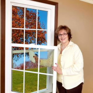 Woman cleaning vinyl-frame swing-in window while smiling.