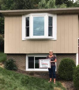View of satisfied customer of Energy Swing Windows holding sign in front of new installed vinyl replacement windows.