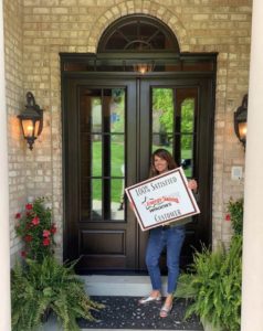 Satisfied customer posing for photo in front of her newly installed woodgrain front entry doors.