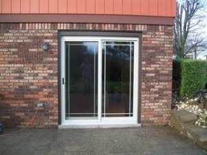 Exterior view of residence with brick walls and white frame sliding patio doors. Blue skies in background.