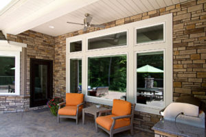 Outdoor living area with two chairs, an outdoor grill, and seven white-frame vinyl replacement windows.